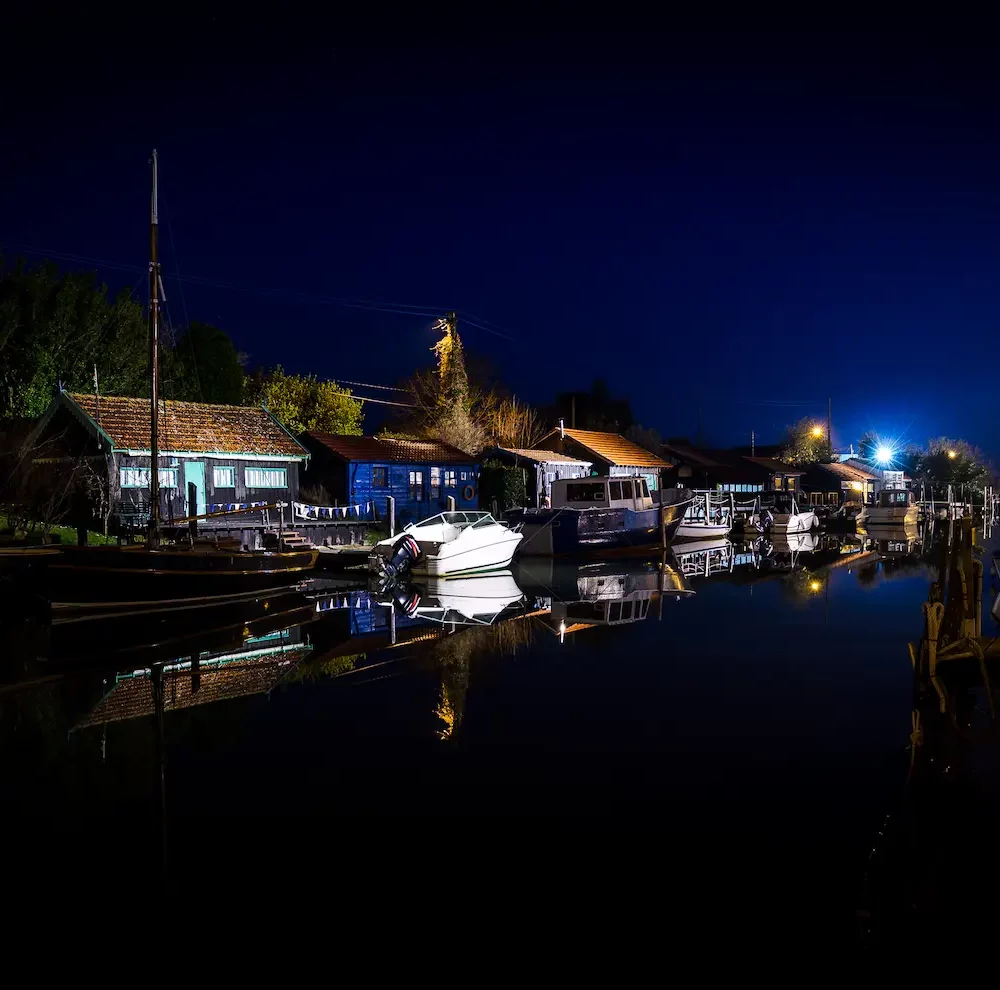 Port de nuit avec bateaux amarrés et lumières.
